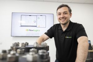 Smiling man in a black shirt standing beside industrial equipment.